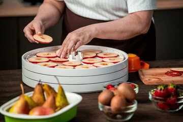 Hands of housewife putting slices of red apples on tray of domestic fruit dryer