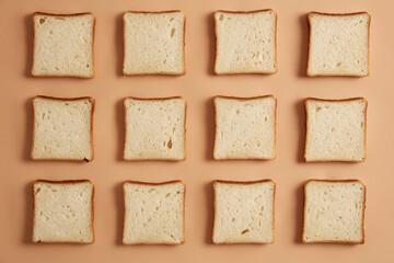 Overhead shot of unroasted bread slices arranged in rows, ready for toasting, isolated on beige studio background. Preparing delicious sandwich. Tasty snack. Sliced bakery product. Flat lay.