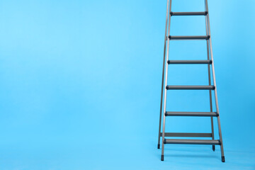 Metal stepladder on light blue background. Space for text