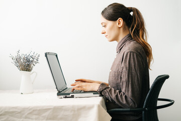 young woman,working from home during virus quarantine,on her laptop.girl is sitting at white table,in minimalistic interior.cosy working place,concept of remote work,concept of minimalism
