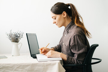 a young woman who works from home while the virus is quarantined on her laptop, studies information on the Internet and writes notes in a diary.cosy working place,the concept of remote work.freelance