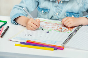 Preschooler draws in his notebook colored markers and pencils