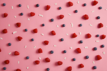 Organic fresh ripe delicious raspberry and blueberry with coconut flakes on rosy background. Yummy healthy dessert. Collage from tasty berries. Harvest concept. Top view. Mix of summer fruits.