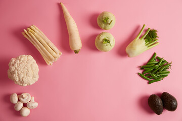 Top view of seasonal vegetables on pink background. Fresh mushrooms, broccoli, asparagus, radish, fennel, peas and ripe avocado. Healthy diet concept. Copy space in middle of shot for your text