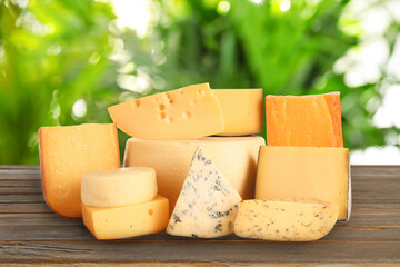 Different types of delicious cheeses on wooden table outdoors. Dairy products