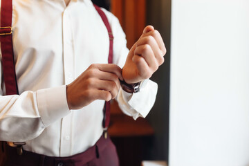 Fototapeta na wymiar A groom putting on cuff-links as he gets dressed in formal wear. A man straightens cufflinks. Groom's suit