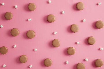 Overhead shot of delicious macaroons of brown color arranged on pink background with marshmallow. Traditional french dessert. Sweet gourmet cookies for eating. Breaking diet. Confectionery product