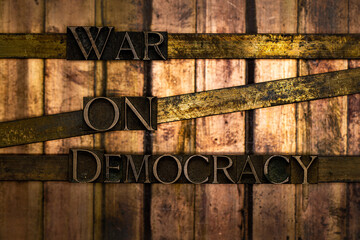 Photo of real authentic typeset letters forming War On Democracy text on vintage textured silver grunge copper and gold background