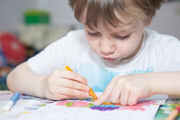 Portrait of a child who carefully paints the picture at home with felt-tip pens. Development of fine motor skills and creative abilities in children.