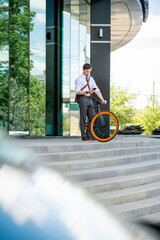 Elegant businessman with smartphone and bicycle standing by open door