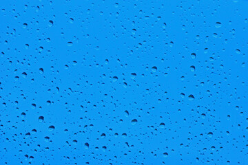 Krople wody na szybie okiennej z niebieskim tłem w deszczowy dzień  - obrazy, fototapety, plakaty