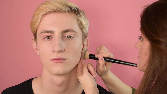 makeup for men, makeup artist does makeup, paint with  brush, handsome man, makeup artist with red hair, pink background    