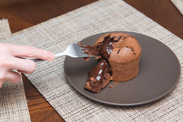 female hand breaks with a fork homemade chocolate fondant and chocolate flows from it