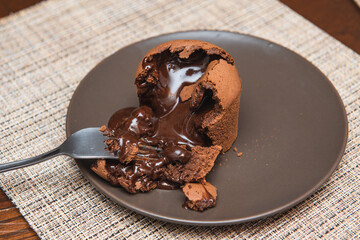 .close up veiw of hot chocolate flows from a chocolate fondant onto a brown plate