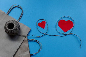 Craft packaging bag with hearts and twine. Flatley on blue background with Copy space. Gifts for holidays, Valentine's day and birthday with love. The concept of love, greeting, flat lay.