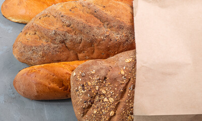Freshly baked bread and baguette in a paper bag on a gray textural background.