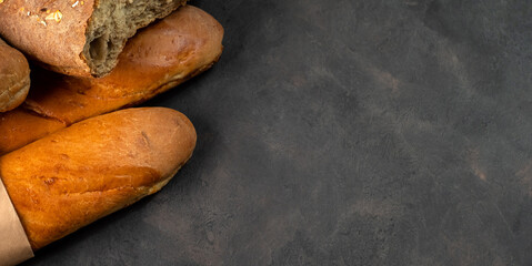 Fresh appetizing baguette with a crispy crust on a dark background. Free space on the right, baguette on the left.