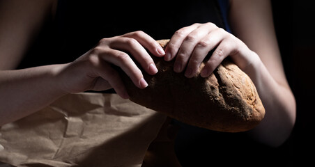 Hands cracking delicious fresh bread taken out of a paper bag. Dark background.