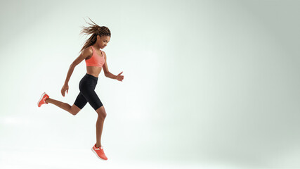 Fototapeta na wymiar No limits. Full length of young african woman with perfect body in sports clothing jumping against grey background while training in studio