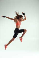 Just never stop. Full length of young african woman with perfect body in sports clothing jumping in studio against grey background