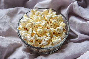 transparent glass bowl with popcorn on a gray blanket. watching movies at home