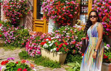 Indian lady with black curly hair wearing a greek style gown in summer in Europe with lot of flower background.