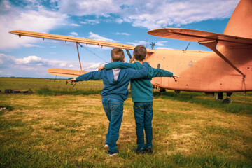 Two boys are standing and watching the plane