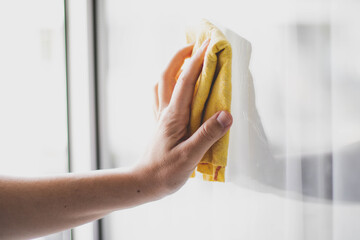 Die Putzfrau hat ein gelbes Tuch in der Hand. Die Frau wischt das Glas mit einem gelben Tuch ab.