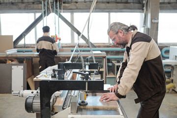 Grey-haired worker of factory going to process board on industrial machine
