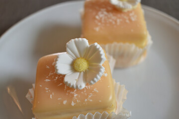 Pie Petit four with sugar flower and coconut shavings on a white saucer.