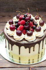 Birthday cake decorated with melted chocolate, whipped cream and fresh cherries. Rustic wooden background.
