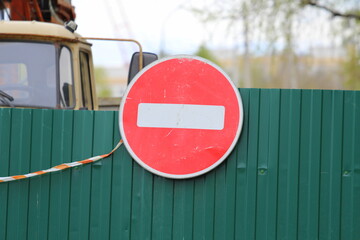 Red round road sign with white stripe prohibiting movement on the green fence of sheet iron. Do not...