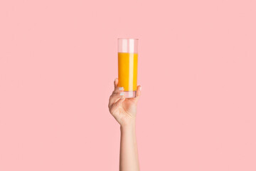 Millennial woman showing glass full of orange juice on pink background, closeup