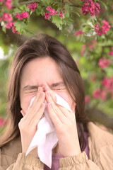 Young girl is blowing her nose near spring tree in bloom. Health and medicine concept