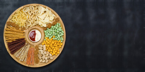 Assortment of snacks for beer on a wooden plate. Black wooden background.