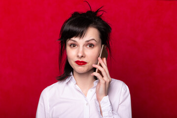woman in a white shirt speaks on the phone, red lips, red background