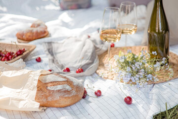 Aesthetic picnic outdoors with wine glasses bread berries and flowers. Rustic picnic with neutral tones colours. 