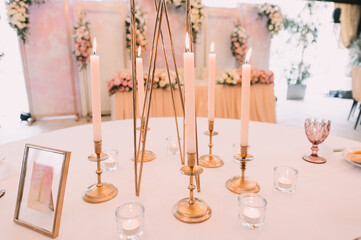 Banquet, restaurant. Table setting. White plates with a gold rim, golden cutlery, glasses. Peach-colored napkin with a golden ring. Peach pink floral arrangements. Tall tapers in gold candle holders