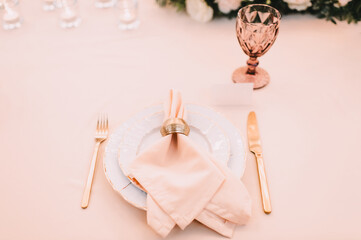 Peach pink floral arrangement. Banquet, restaurant. Table setting. White plates with a gold rim, golden cutlery, glasses. 