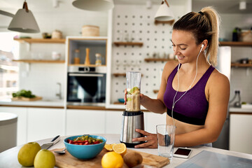 Happy athletic woman preparing fruit smoothie in the kitchen.
