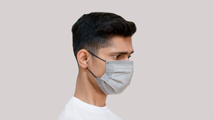 Tensed young asian boy about new virus corona virus covid 19 young doctor side pose on grey background portrait face wearing surgical mask