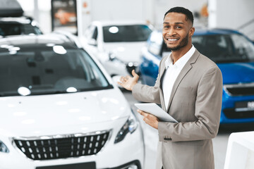 Cheerful Car Dealer Gesturing Showing Brand-New Automobile Standing Indoors