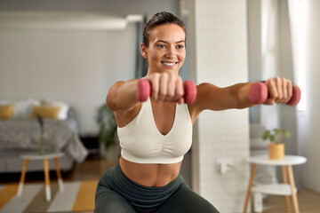 Happy athletic woman practicing with hand weights in the living room.
