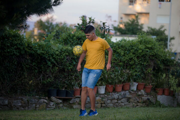Teenager in playing football in a garden.