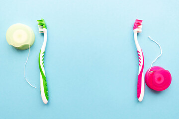 Image of dental floss and two toothbrushes pink and green on sides on light blue backround with a...