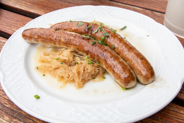 Bratwurst sausage (Brätwurst, brät, Wurst)and sauerkraut traditional German dish/food with garnish/chives on a white plate and wooden table