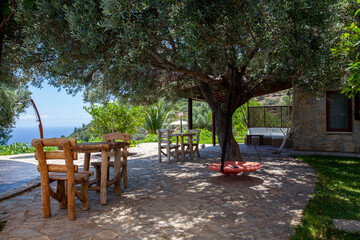 Fototapeta na wymiar Wooden chairs and tables, red swing in a beautiful garden with beautiful trees and sea view.