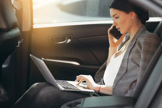 Young businesswoman in suit talking to investors while sitting in a car and checking information through a laptop.