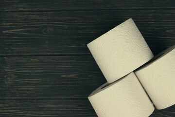 Three rolls of white toilet paper on wooden background with space for text. Deficit means of hygiene during coronavirus
