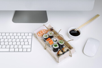 Assorted sushi and rolls near the computer. Eating at the workplace. Home office.